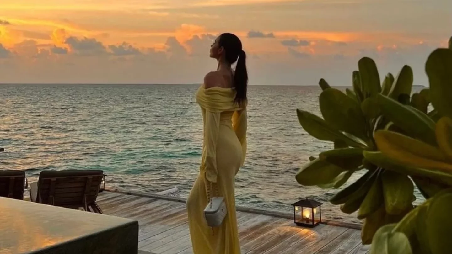 Une femme sur une terrasse en bois en bord de mer habillée d'une robe jaune 